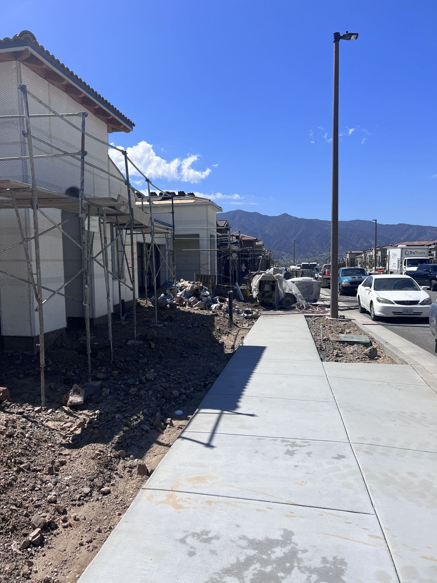 Homes under construction with scaffolding along a hillside street, mountains in the distance