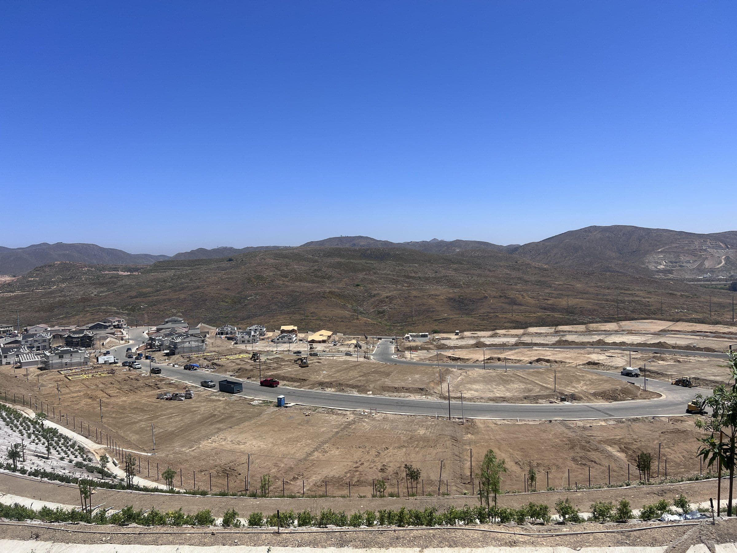 Aerial view of a hillside residential development, with graded lots, new roads, and homes under construction