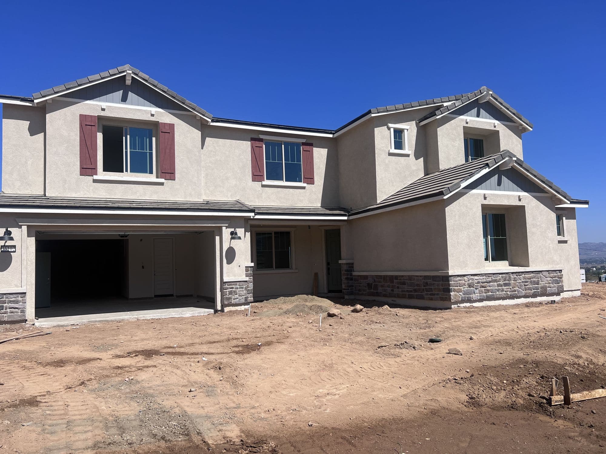 A completed two-story home exterior on a graded lot under a clear blue sky