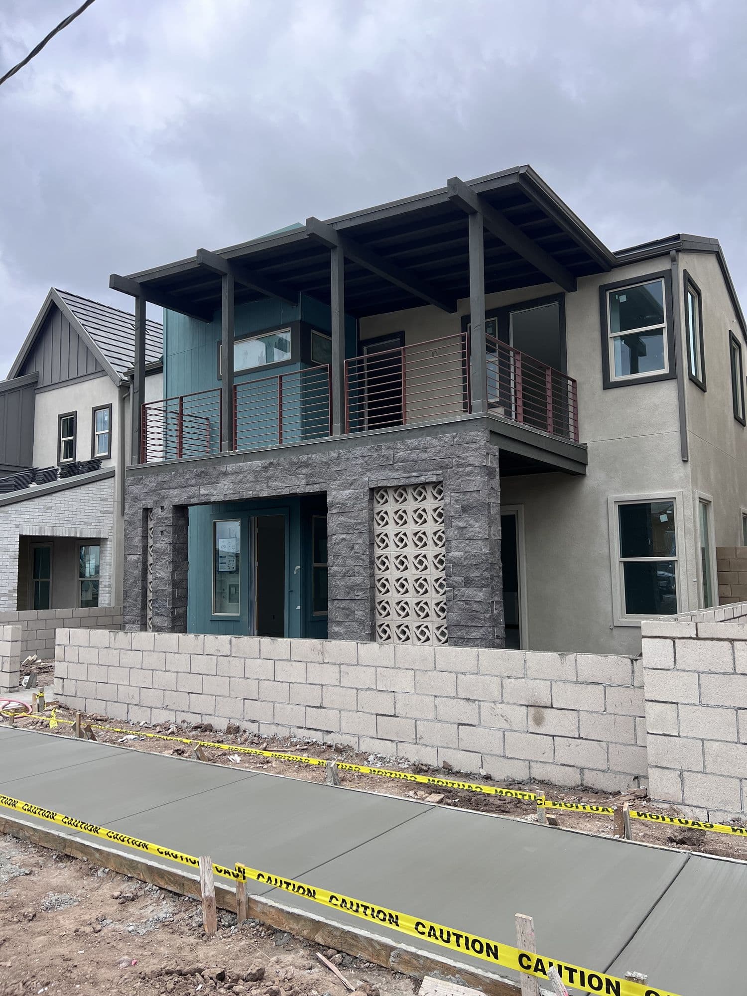 A modern two-story home nearing completion, with stone facade and a fresh concrete sidewalk