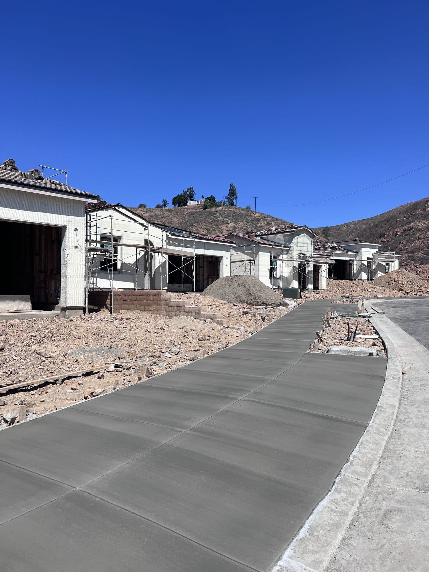 A row of homes under construction with scaffolding, beside a newly poured concrete driveway
