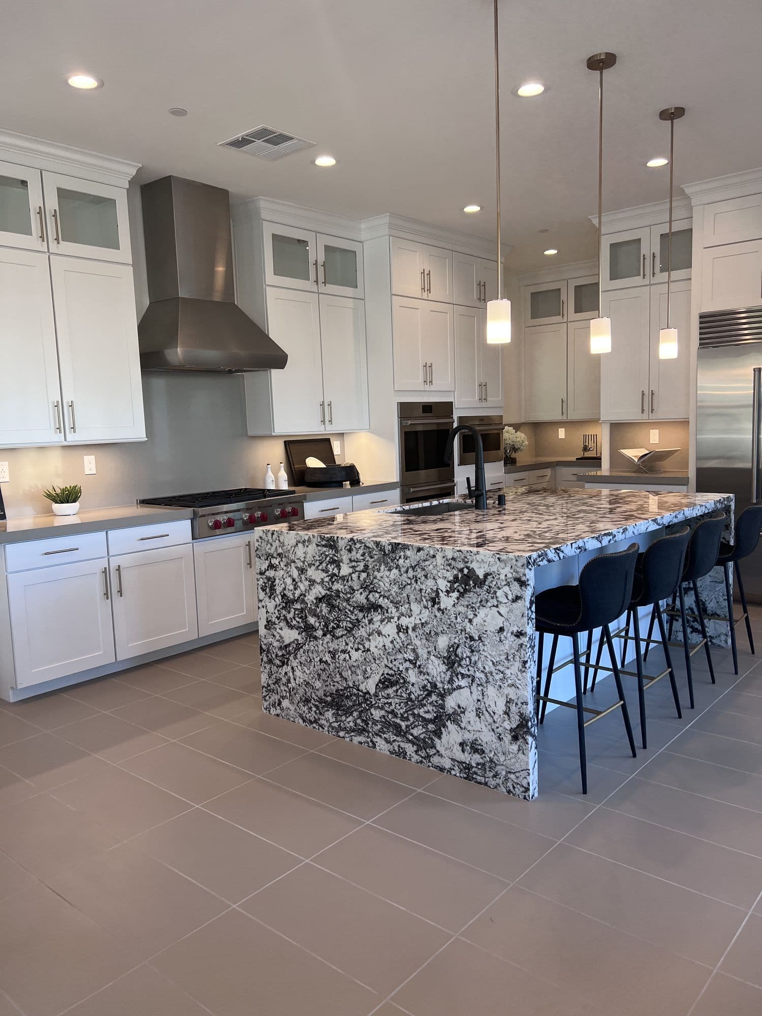 A finished model-home kitchen with white cabinetry and a granite waterfall island